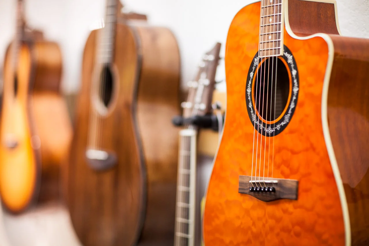 Close-up of an orange acoustic guitar body with sound hole, other guitars blurred in background, warm wood tones
